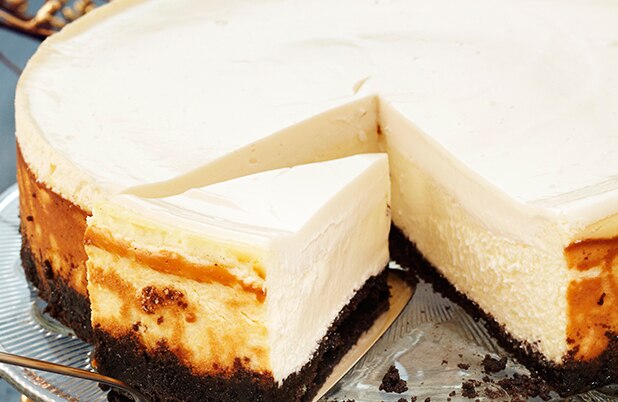 Una espátula levanta una rebanada de pay de queso con corteza de galleta de chocolate.