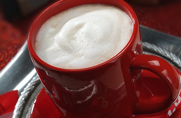 A red mug filled with foam on silver saucer and red napkin.