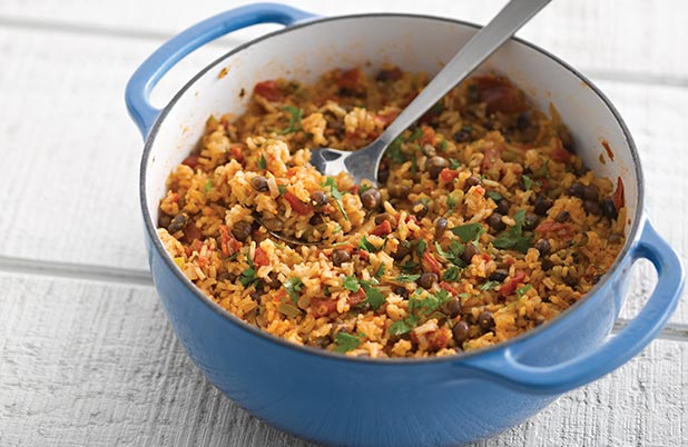 Una olla holandesa azul llena de arroz, guisantes negros, cilantro y una cuchara para servir.