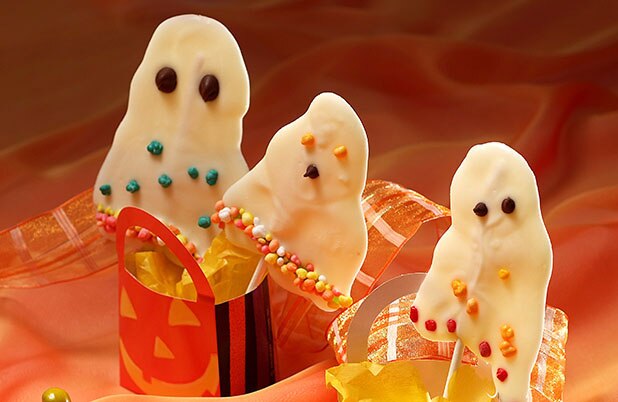Fantasmas de chocolate blanco en palos que sobresalen de las bolsas de Halloween.