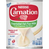 Fotografía frontal de una lata blanca, roja y azul de Leche Evaporada Sin Grasa. Tiene la marca Carnation y el logotipo de la flor, una tapa de botella de plástico azul oscuro, y una imagen de la leche evaporada vertiéndose en una espátula blanca.