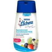 Una botella sirve fácil con una tapa color azul con el logo de La Lechera, junto a una pila de fruta rociada con leche condensada azucarada.