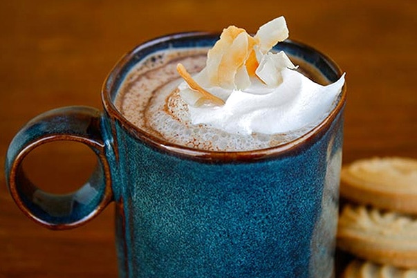 A blue mug filled with Abuelita™ Mexican hot chocolate and whipped cream along with some cookies.