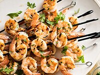Sobrecarga de brochetas de camarones a la parrilla en un plato blanco, adornado con cilantro.