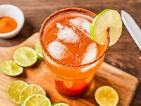 Sobrecarga de michelada en un vaso de cerveza sobre una tabla de cortar de madera con limas cortadas alrededor.