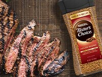 Sobrecarga de café instantáneo Taster's Choice junto a un bistec de flanco marinado con café en rodajas sobre mesa de madera.