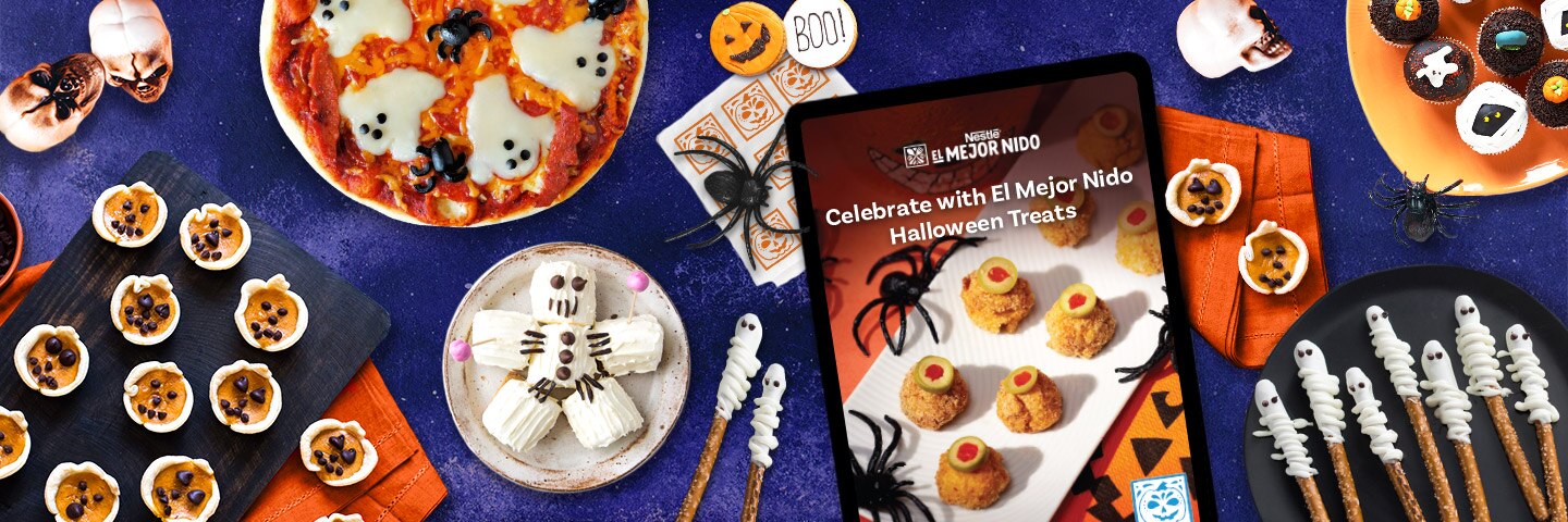 Pretzels y pizza con temática de fantasmas, hombres de malvavisco, galletas de calabaza, arañas y calaveras junto a una tableta con un libro de recetas en ella.