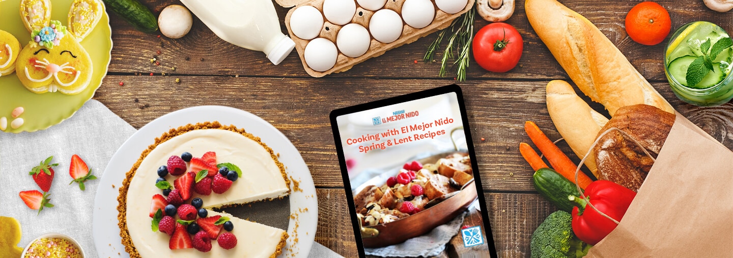 Tableta con recetas de primavera junto a leche, frutas, verduras, huevos, pan, galletas y pastel sobre un fondo de madera.