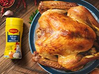 Un pavo asado en un plato azul y blanco al lado de un contenedor de Maggi en una superficie de madera.