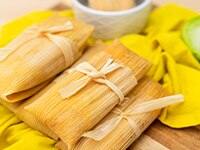 Green Chicken Tamales wrapped and tied in corn husks sitting on a bright yellow table napkin.