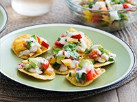 Fish ceviche with pears, chiles and tomato on tortillas rounds on a green plate.