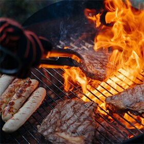Primer plano de un par de tenazas volteando bistecs sellados que se asan a la parrilla.
