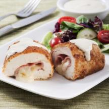 Chicken Cordon Bleu on a white plate with a green salad behind it, on a green place mat, knife and fork in background.