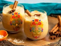 Pumpkin horchata in skull candy glasses next to herbs and rice on a wood surface.