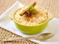 Porridge with a cinnamon stick and star anise on top in a green bowl on a wicker surface.